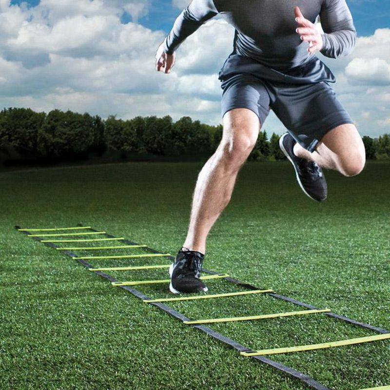 Athlete driving through an agility ladder on a grass field